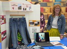 Jackie, Co-Founder of Vulture Collective, is seen smiling from behind a table displaying information related to the business during a end of accelerator program celebration and award ceremony.